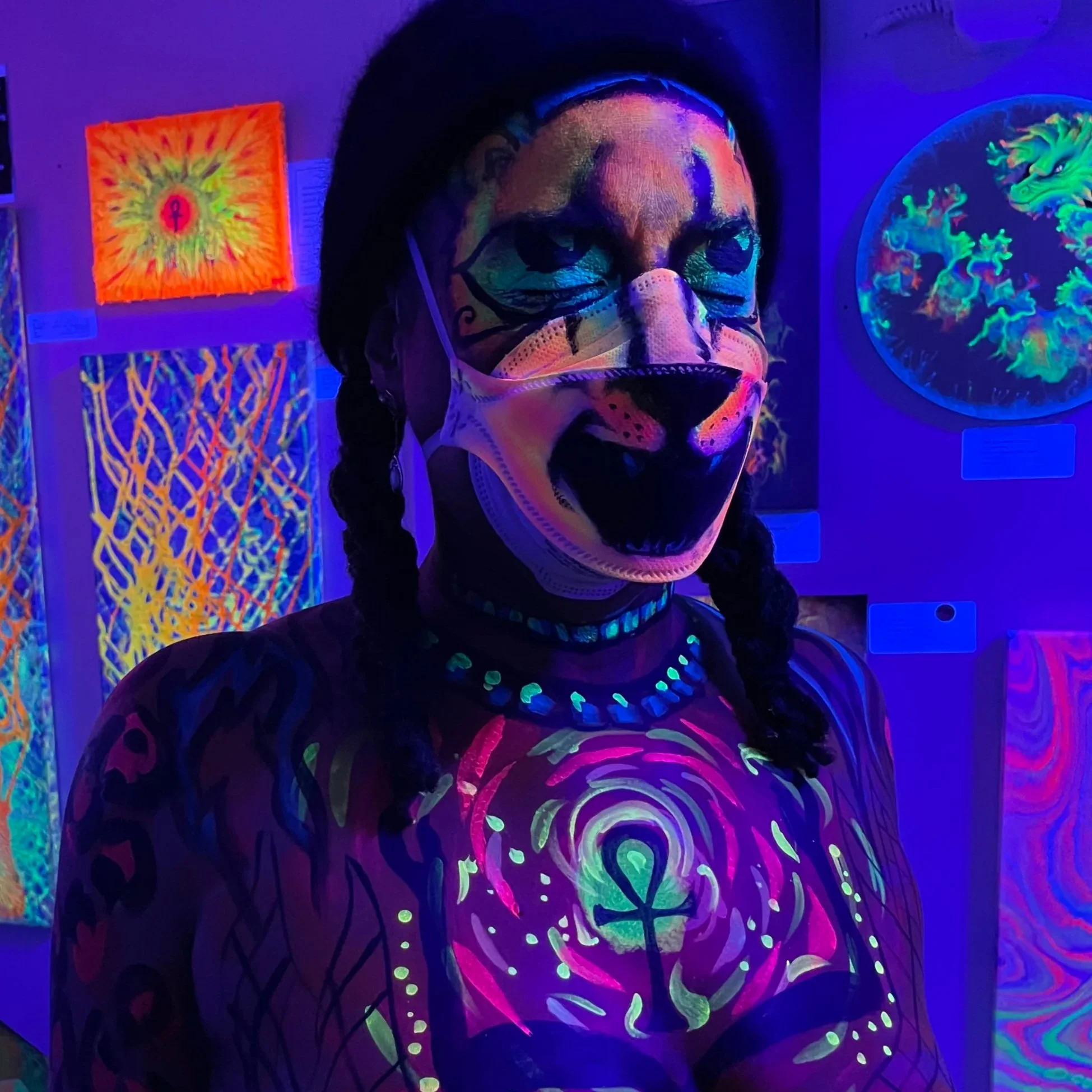 Ali Montgomery dancing before her painting “Sol’s Soul,” illuminated under black light. Her face is painted with lioness features, and her chest is painted with a glowing ankh.