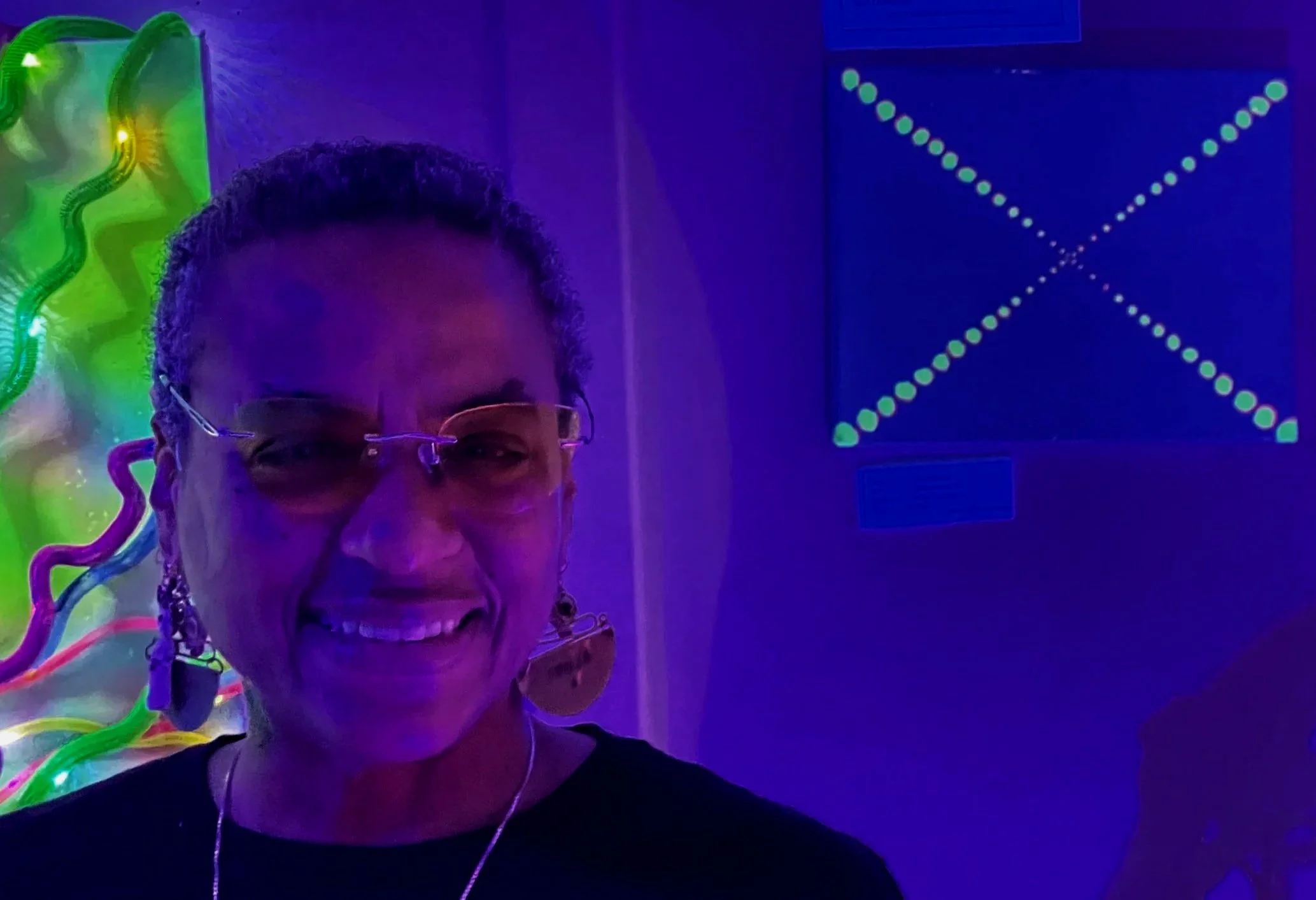 Close up of Ali Montgomery's face before her painting “Bastet's Dream,” illuminated under black light.