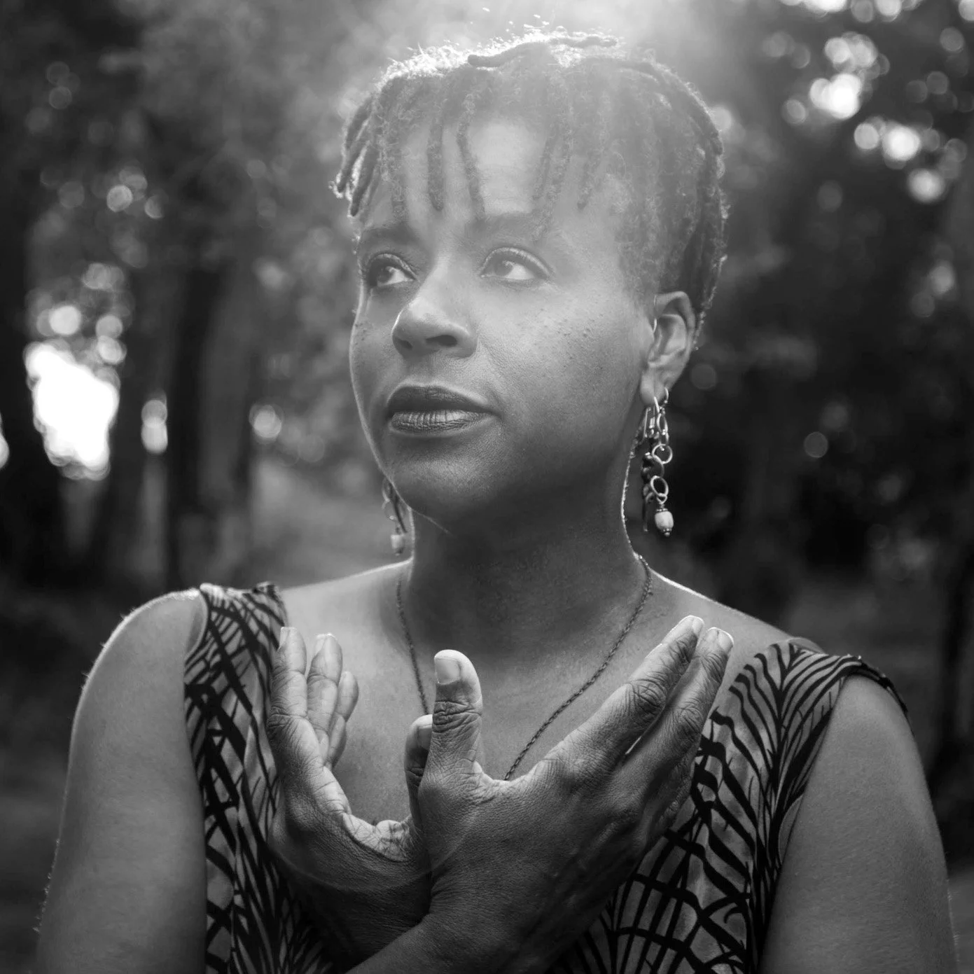 Black-and-white portrait of Ali Montgomery standing outdoors with sunlight filtering through trees. Her posture conveys calm presence, embodied awareness, and the grounded, symbolic clarity she brings to her spirituality based coaching.