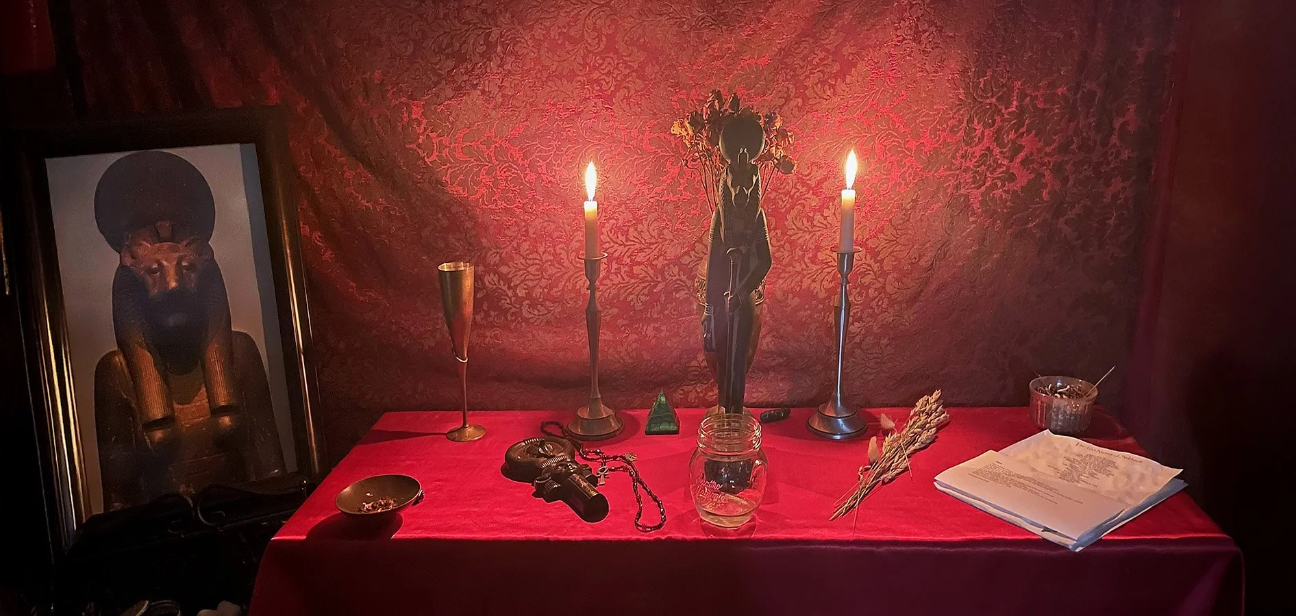 Altar arrangement for a past Sekhmet ritual at Nevermore Oakland, featuring a statue of Sekhmet with candles, ritual tools, offerings, and a red‑draped backdrop, preserved as part of the Temple Memories archive.