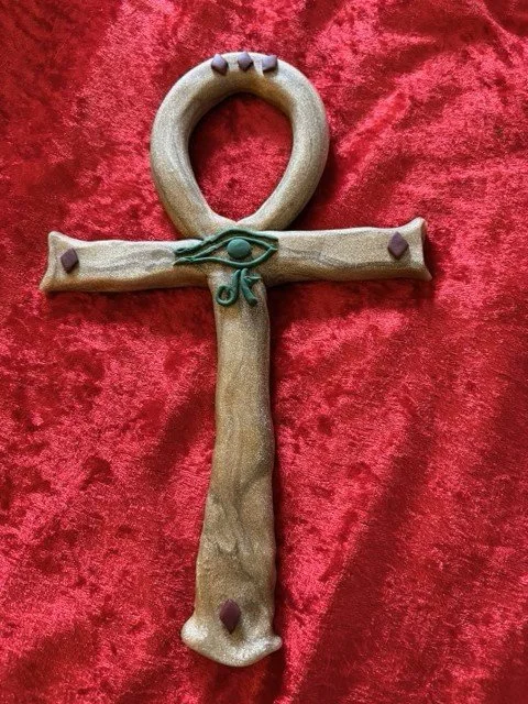 Brown clay ankh with an applied udjat eye on a red velvet background.