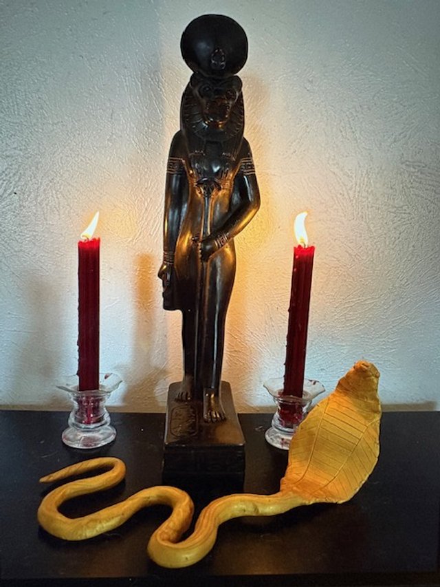 Home altar with a Sekhmet statue, two red candles, and a yellow clay snake wand.