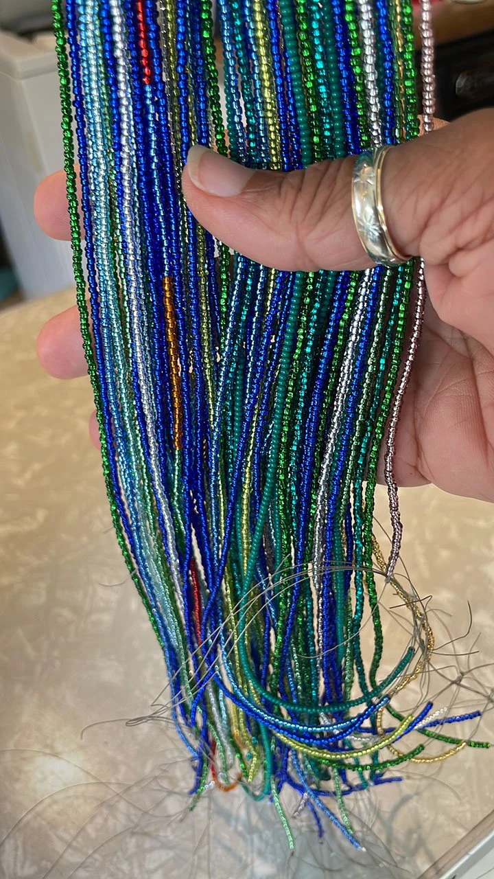 Close‑up of a hand holding many strands of blue and green seed beads.