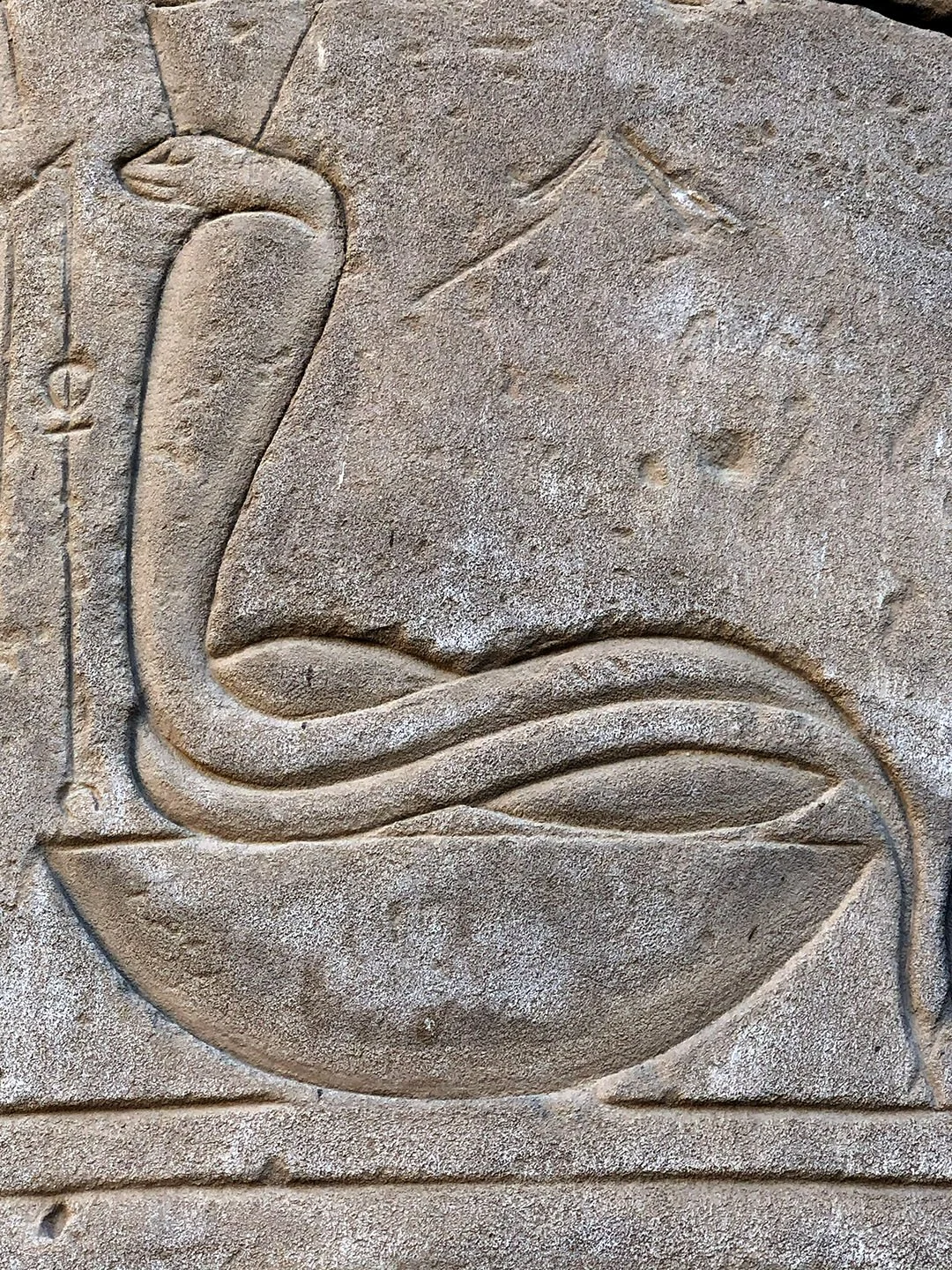 Ancient Egyptian wall relief of a crowned cobra rising from a base, carved in stone at Karnak Temple.