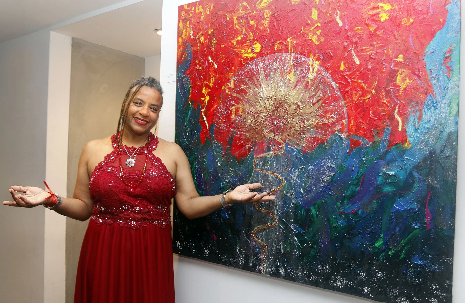 Ali Montgomery, artist and priestess, standing before her painting Ascending the Priestess Path with her arms open in a welcoming gesture.