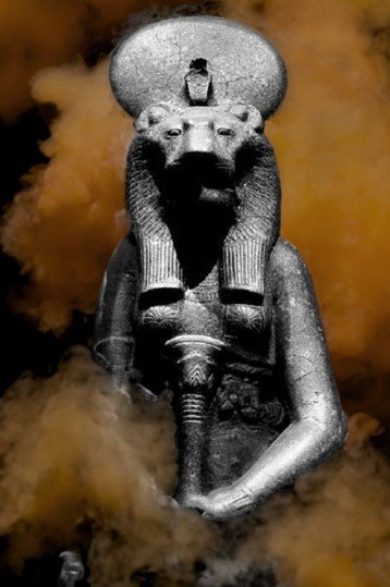 Stone statue of the lion‑headed Goddess Sekhmet shown in frontal view, with soft brown smoke rising around the figure. The sculpture includes the sun disk and uraeus, and the added smoke creates a dramatic, atmospheric effect.