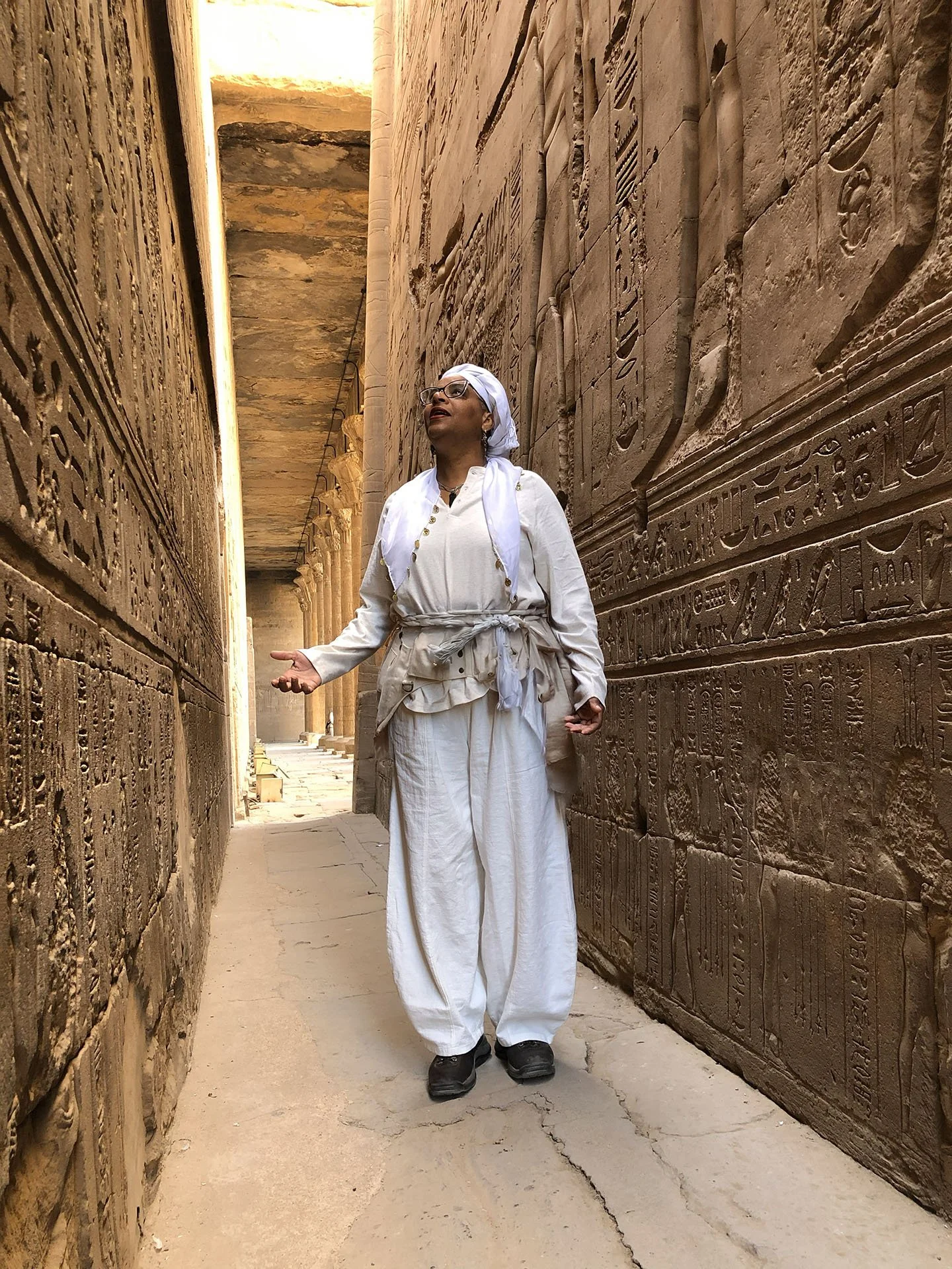 Ali Montgomery standing in a narrow Karnak Temple corridor with walls covered in hieroglyphic inscriptions.