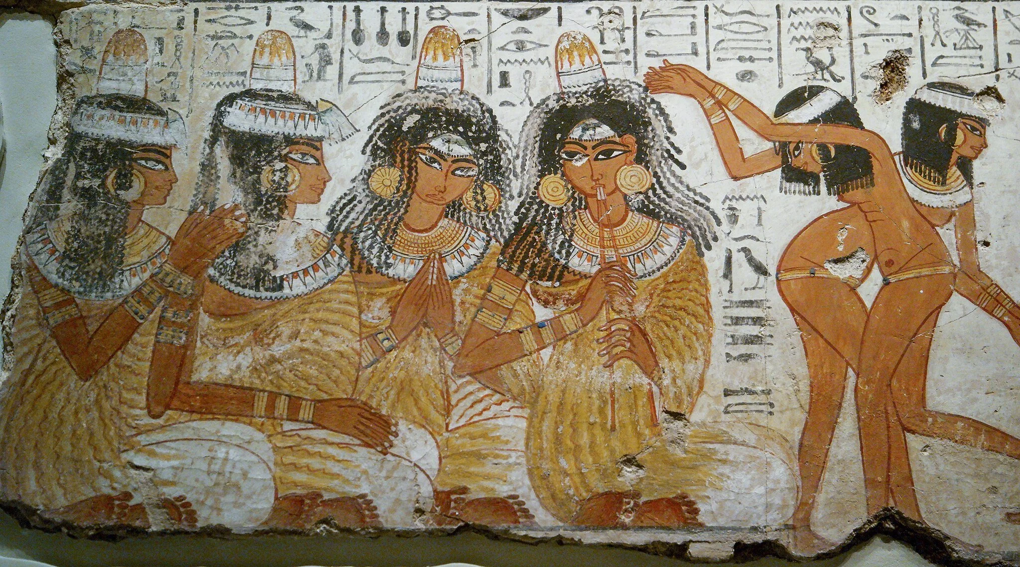 Ancient Egyptian wall painting from the Tomb of Nebamun showing a ceremonial scene with four seated women and two dancers. The seated women wear elaborate wigs, jewelry, and traditional garments, and one plays a flute-like instrument.
