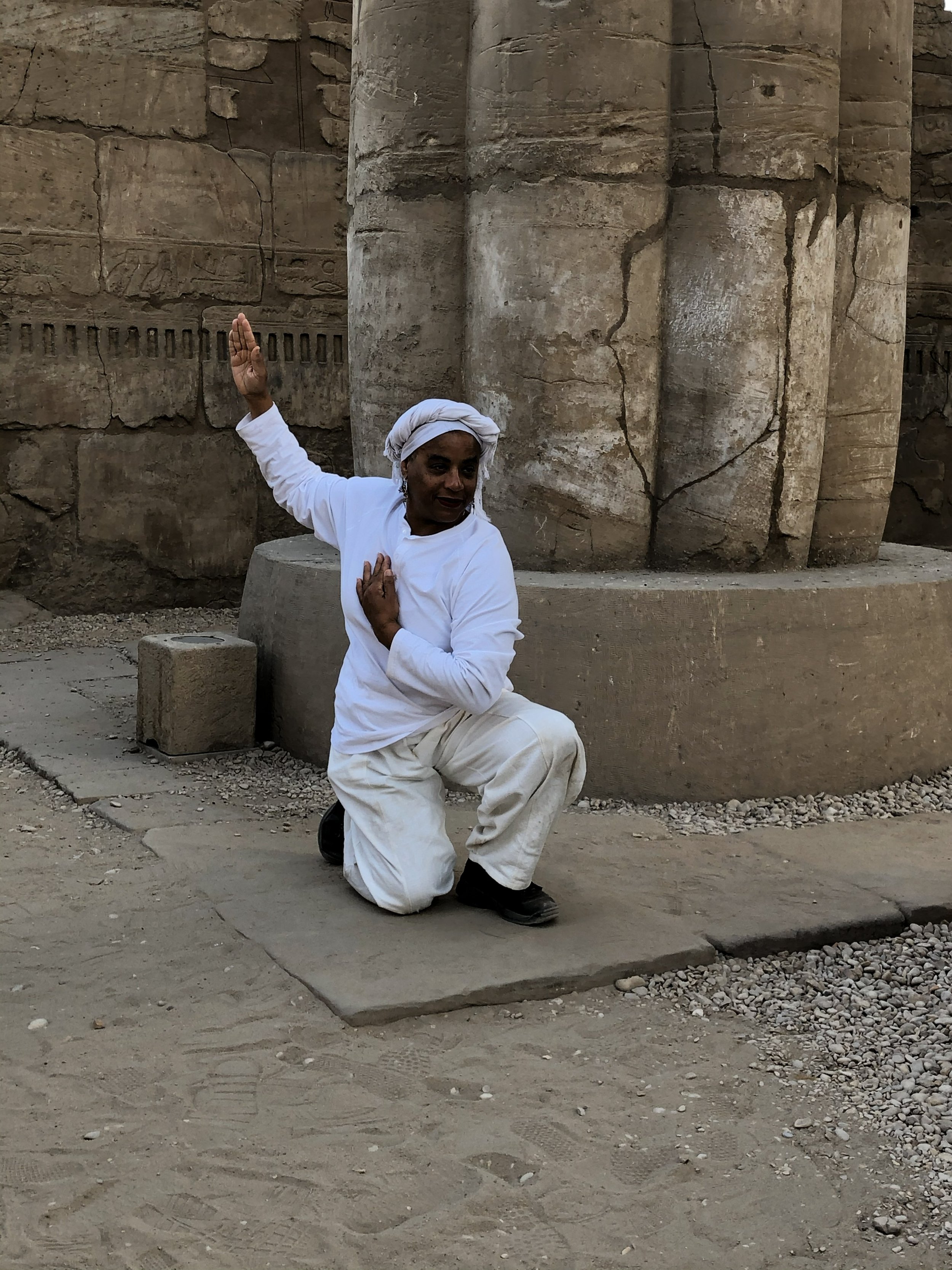 Ali Montgomery in white ritual garb holding a Kemetic Yoga pose in front of a barrel‑fluted stone column at Karnak.