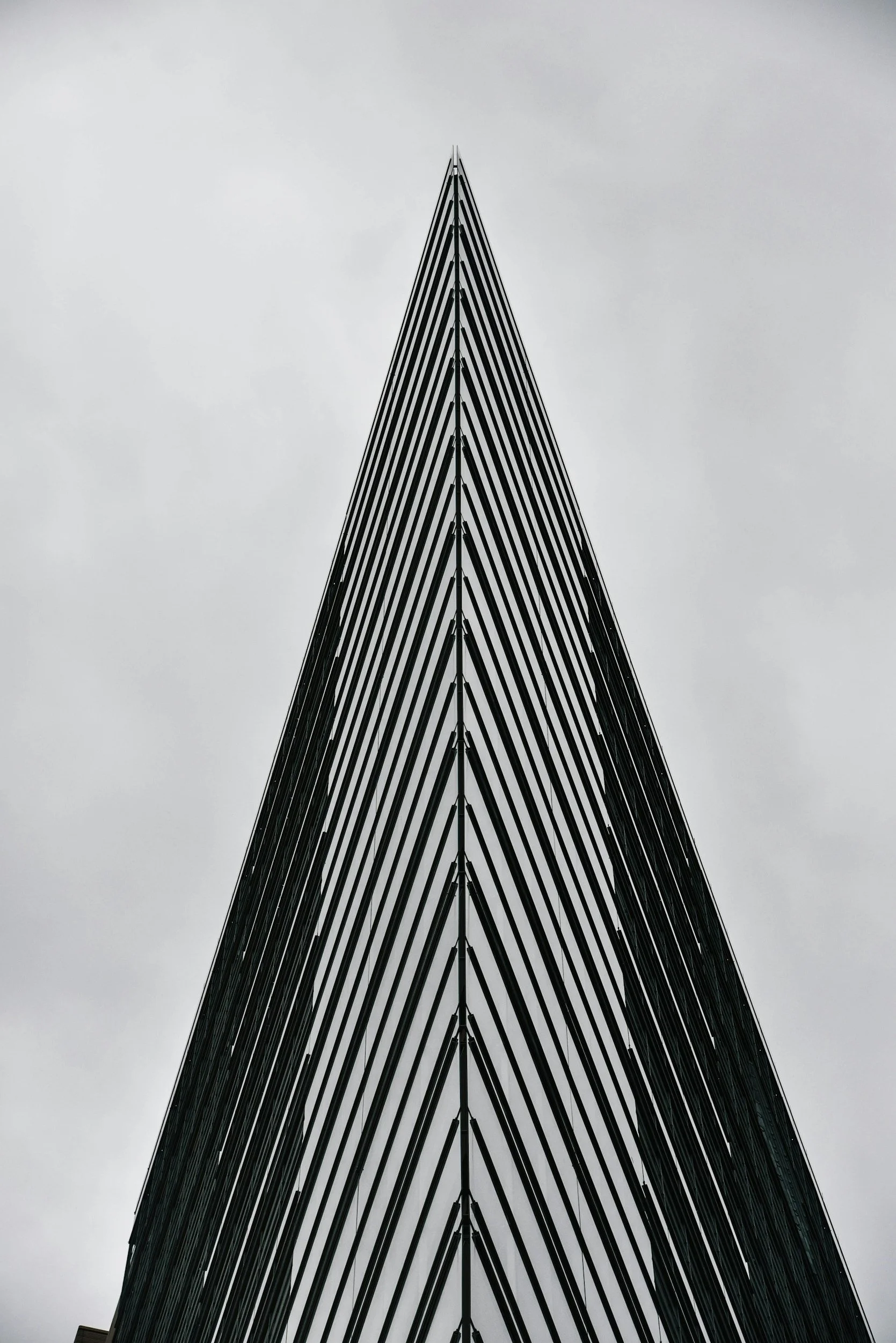 Low-angle view of a modern glass skyscraper with sharp, pointed peak against cloudy sky.