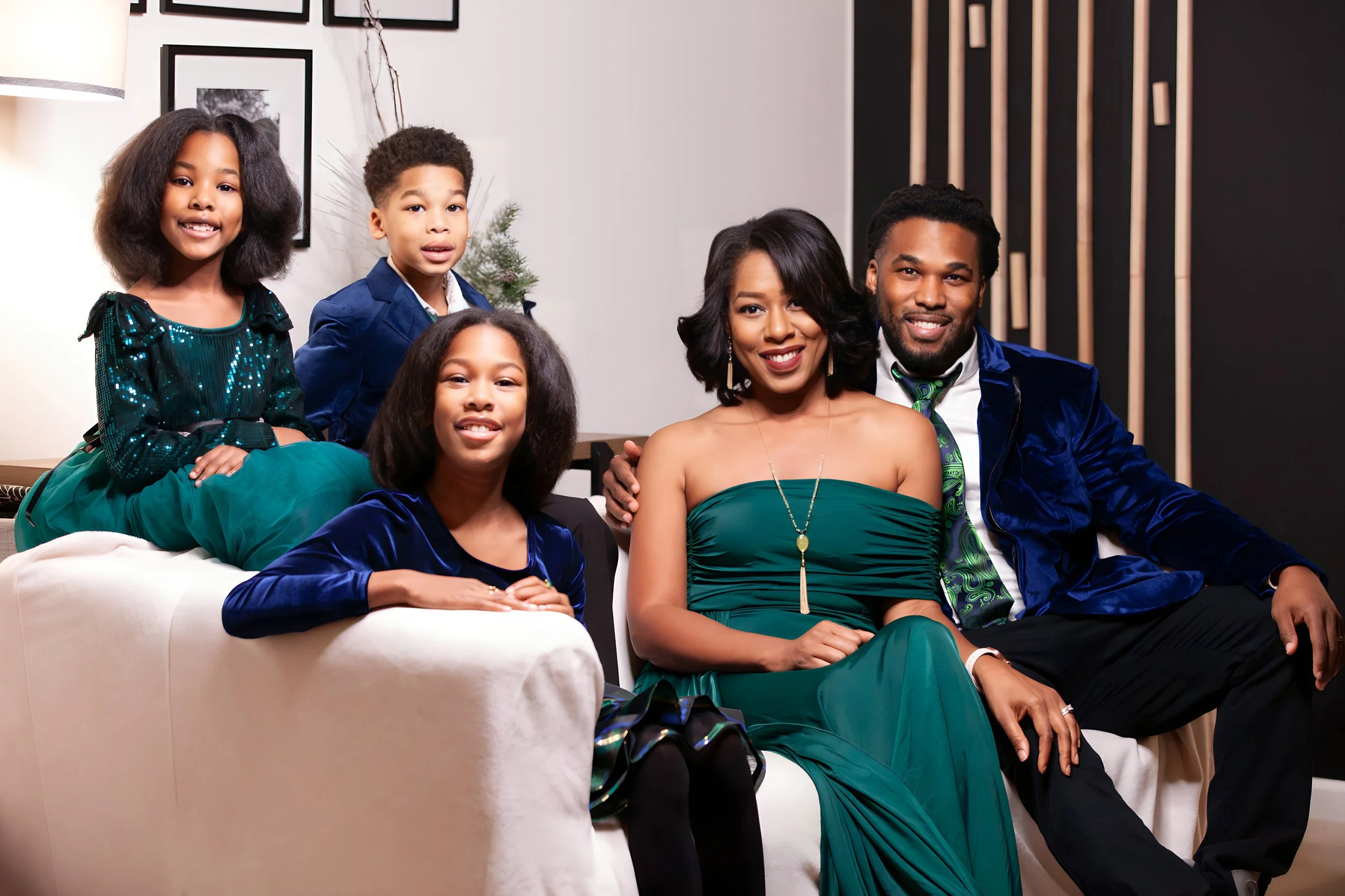 Family of five sitting on a white couch, smiling, dressed in formal attire, in a modern living room.