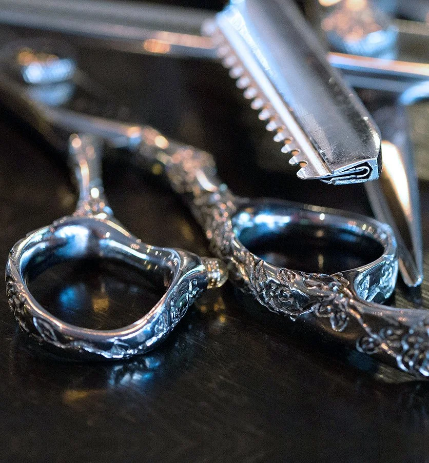 Close-up of a pair of ornate silver rings and a beard trimmer on a black surface.