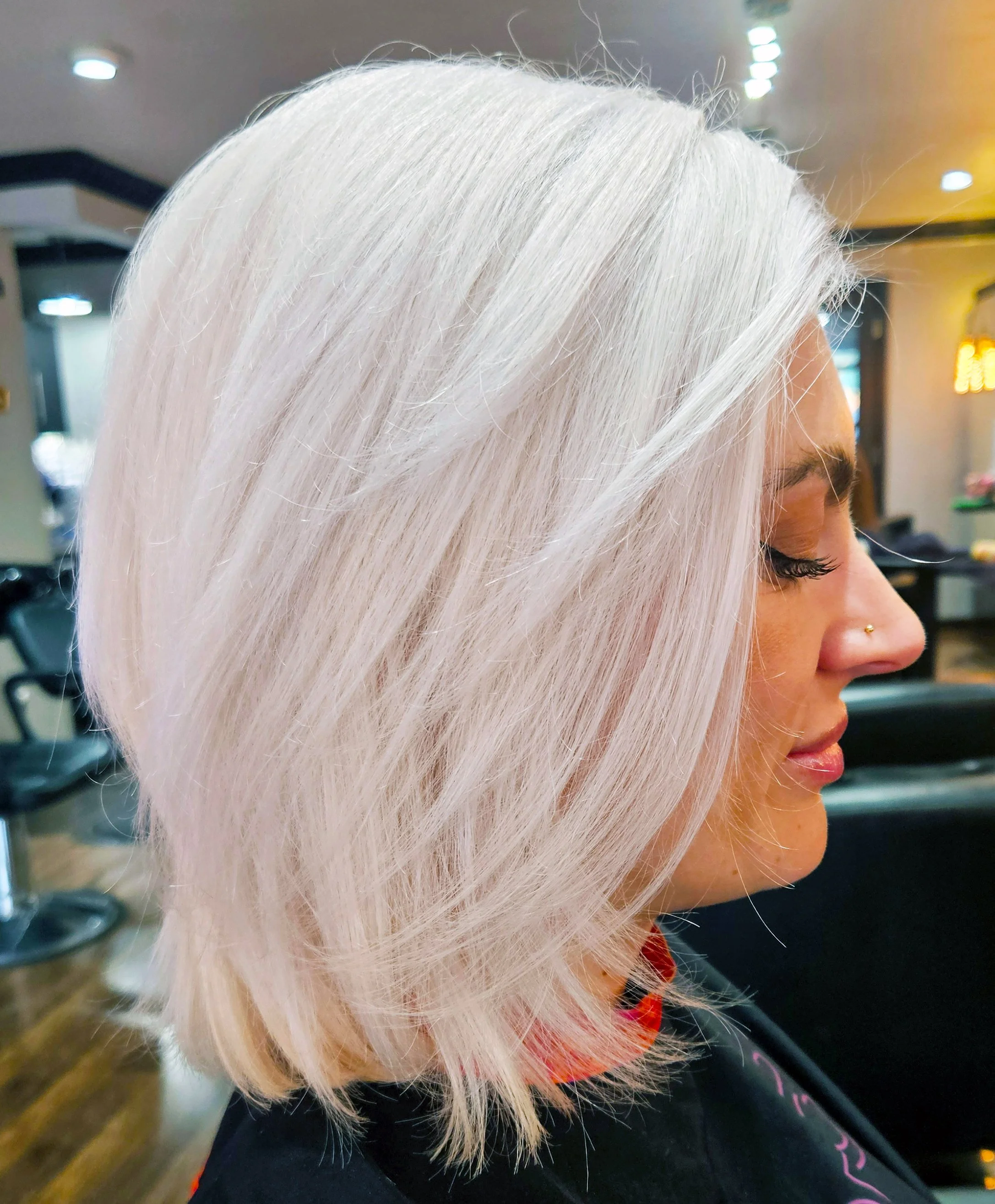 Woman with platinum blonde, layered bob haircut sitting in a salon.