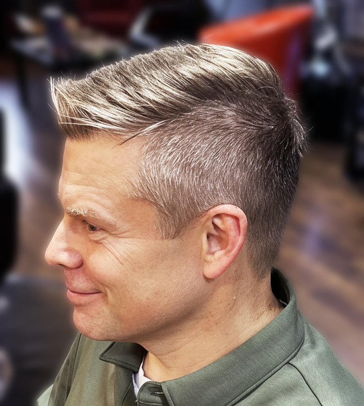 Side profile of a man with short, styled blonde hair, smiling, in a salon or barbershop.