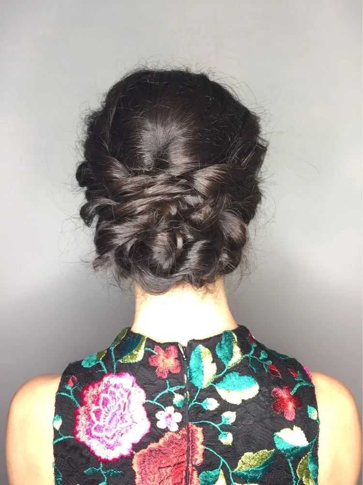 Back of a woman's head with dark, styled hair in loose curls, wearing a black floral embroidered dress with pink, red, and green patterns.