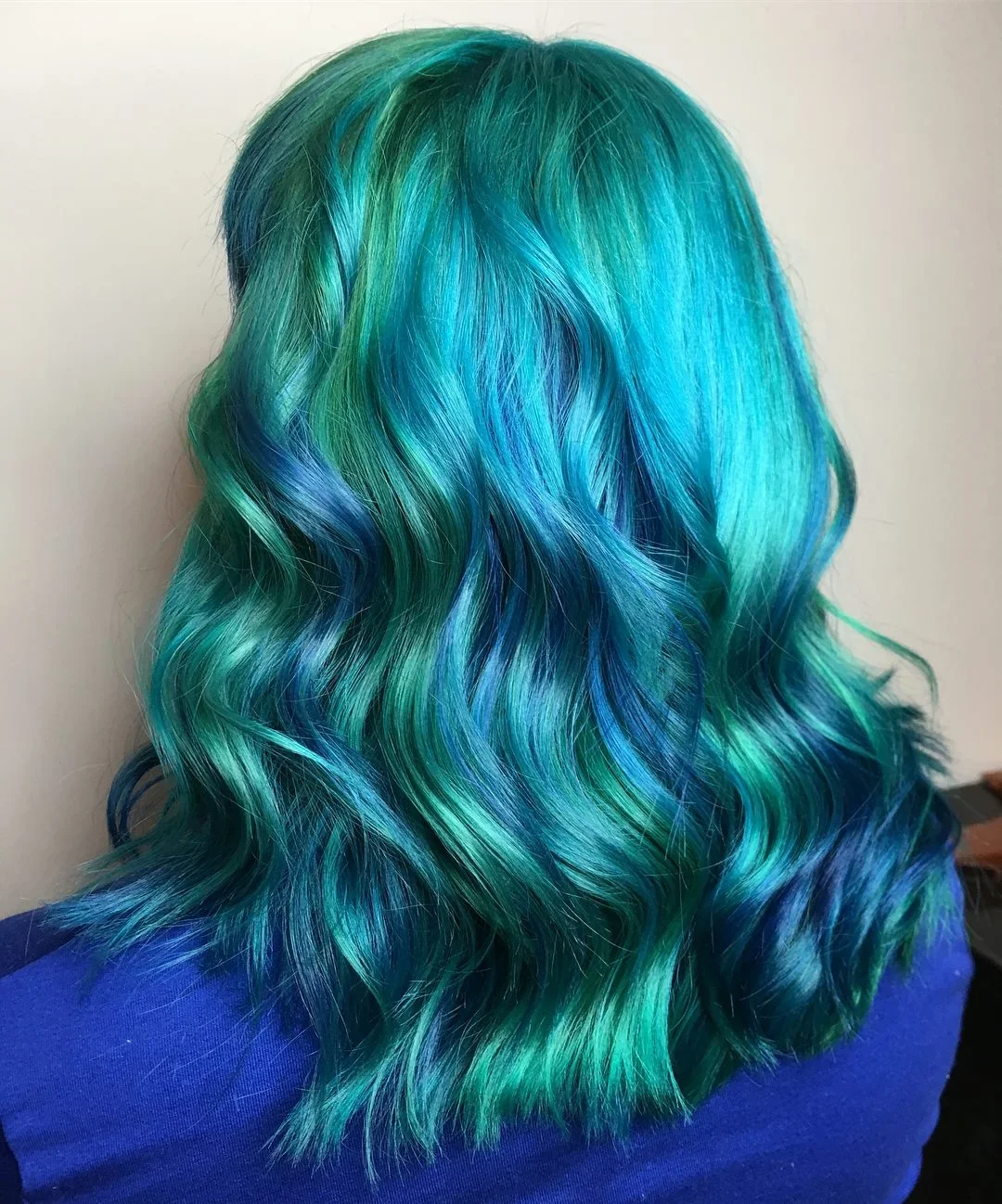 Back view of a person's hair styled in loose waves, with vibrant shades of green, teal, and blue.