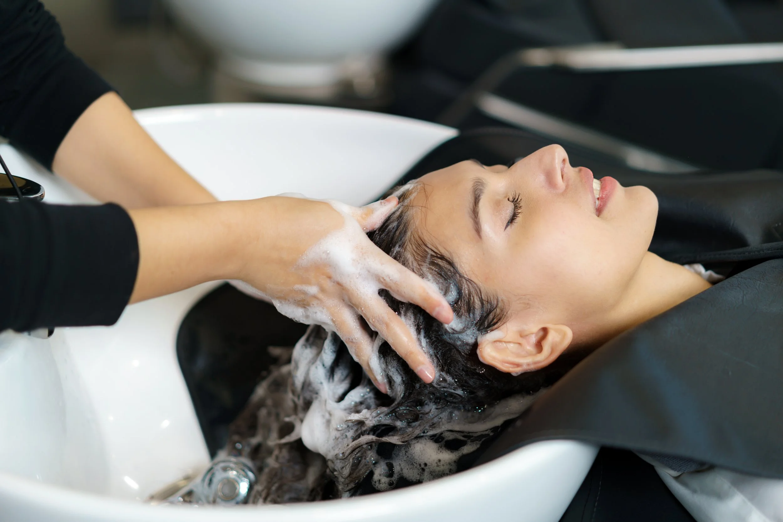 Woman receiving a shampoo in a salon sink while lying back with eyes closed.