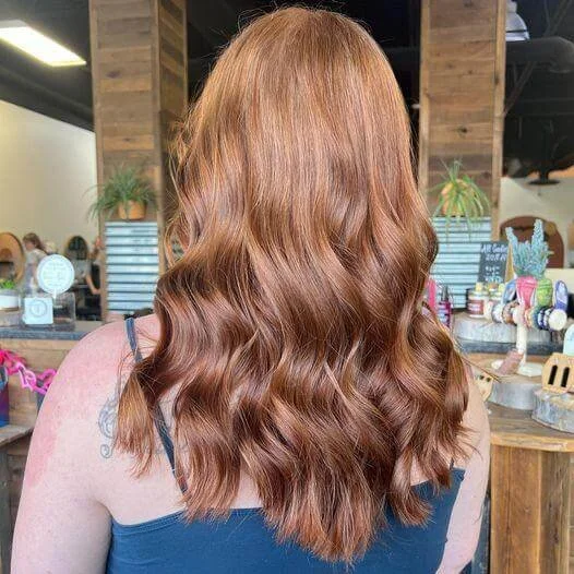 Back of a woman with long, wavy, auburn hair standing in a salon.