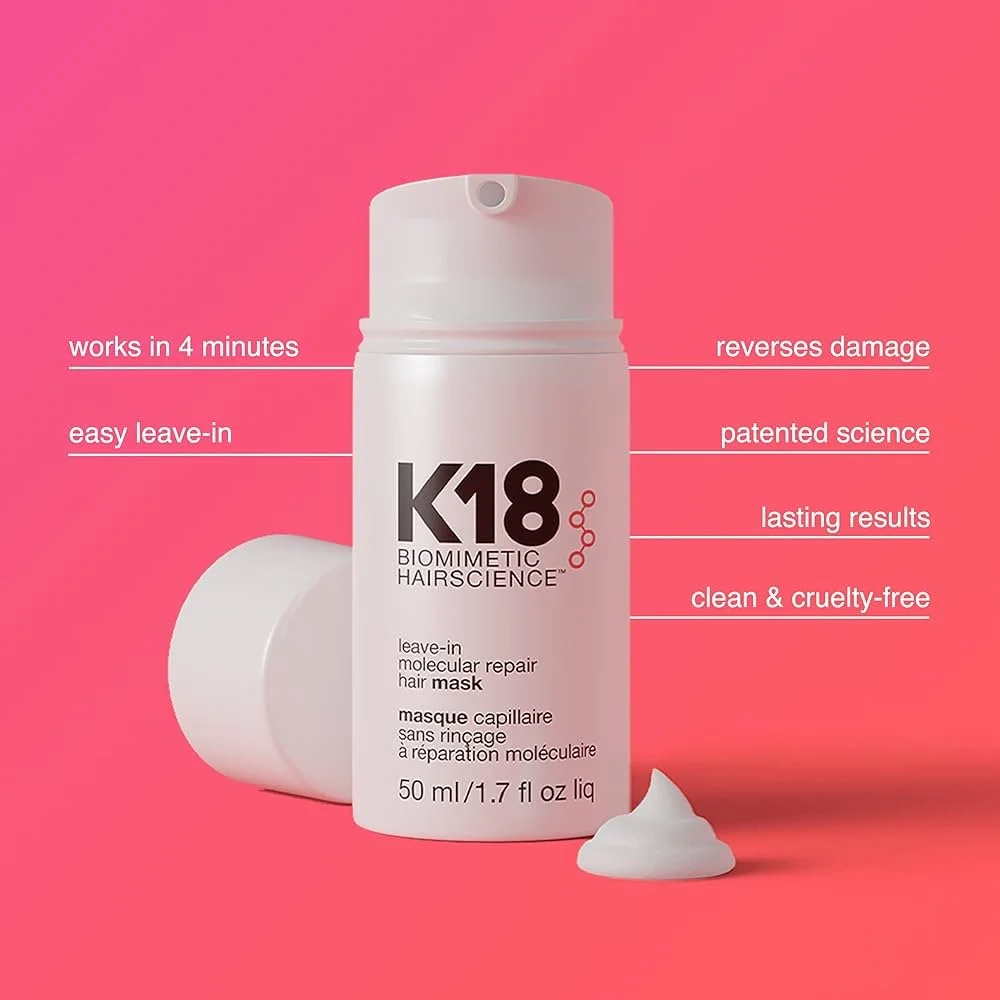 A white bottle of K18 biomimetic hair science leave-in molecular repair hair mask with a pink background, showing its features such as works in 4 minutes, easy leave-in, reverses damage, patented science, lasting results, and is clean and cruelty-free, with some product spilled in front of the bottle.
