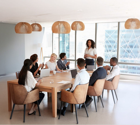 A diverse group of eight professionals in a modern conference room, with large windows overlooking skyscrapers, participating in a business meeting.
