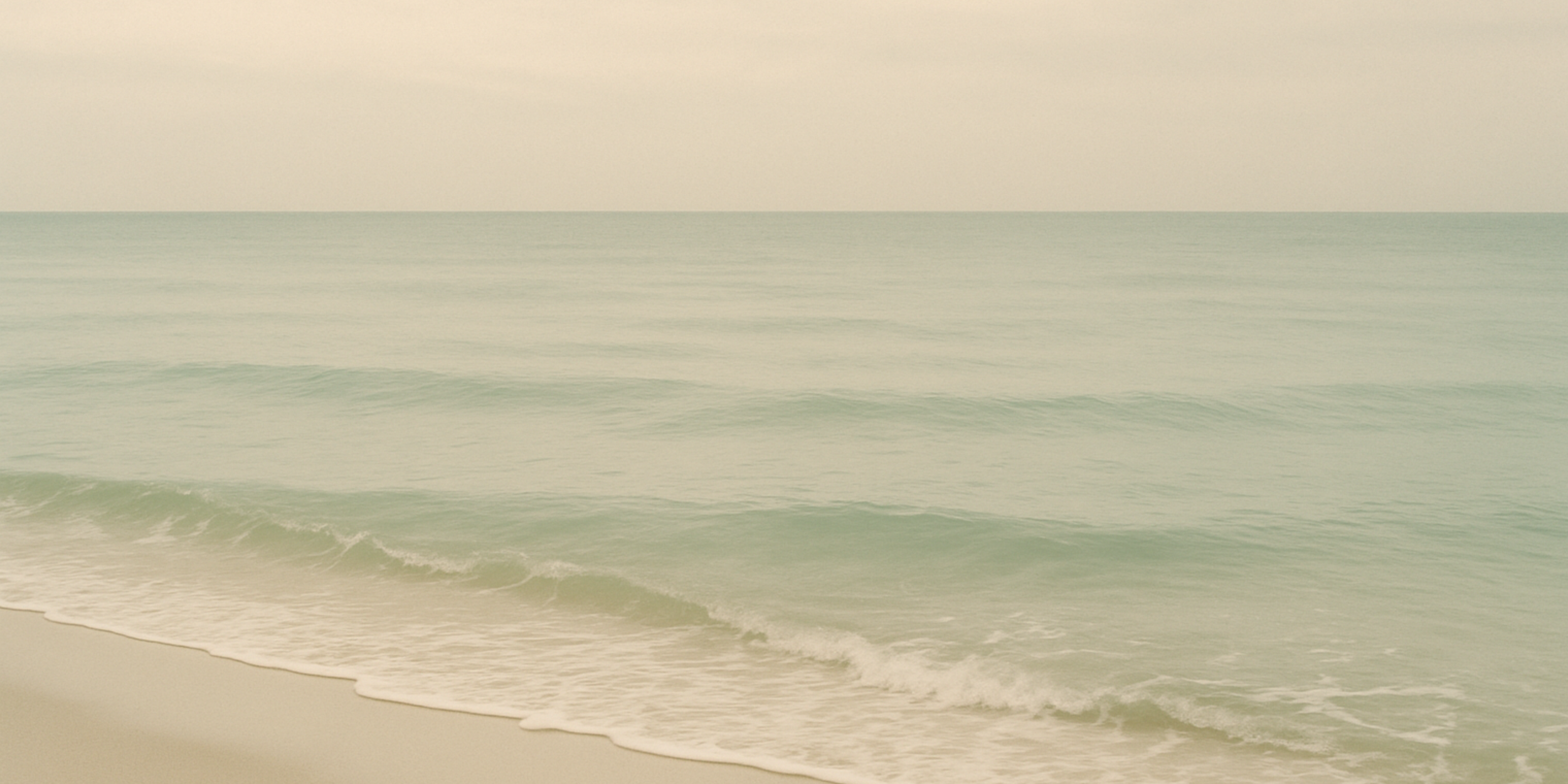Calm ocean with gentle waves reaching sandy beach, overcast sky