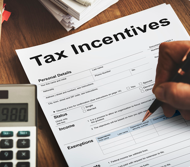 Person filling out a tax incentives form with a pen, next to a calculator on a wooden desk.