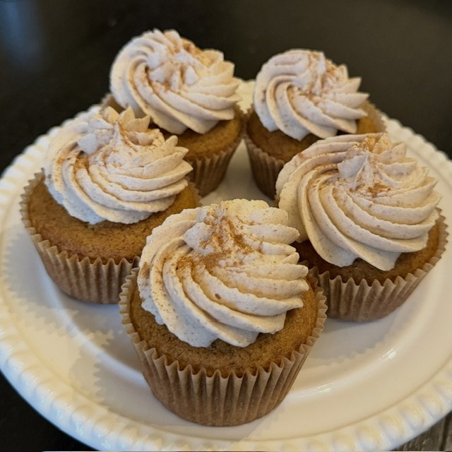 Six cupcakes with swirl frosting on a white paper plate.