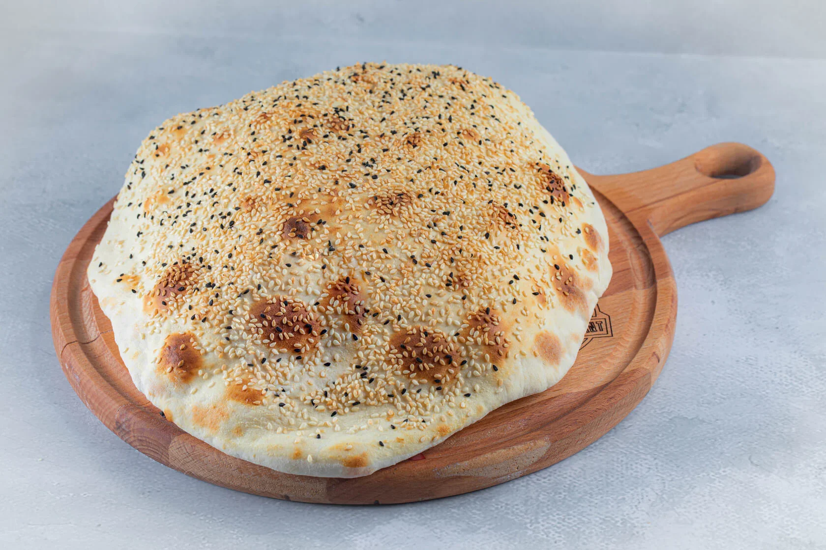 Round flatbread topped with sesame and black sesame seeds on a wooden serving board.