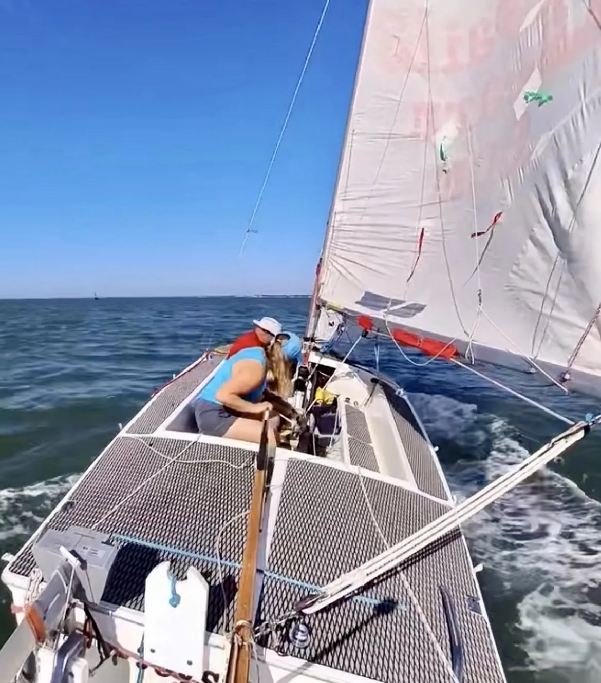 People sailing on a sailboat on the ocean under a clear blue sky.
