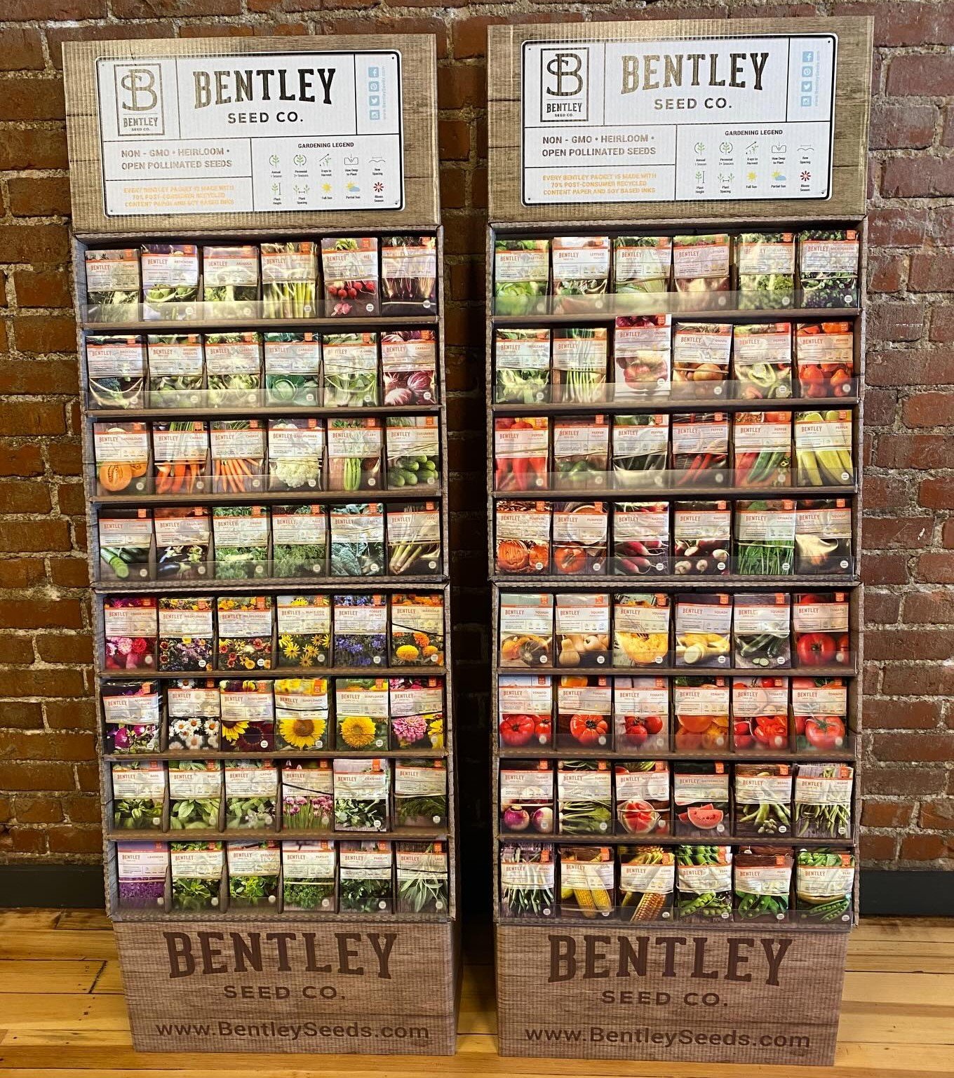 Two display racks of various seed packets from Bentley Seed Co. set against a brick wall, with images of flowers and vegetables on the packet covers.