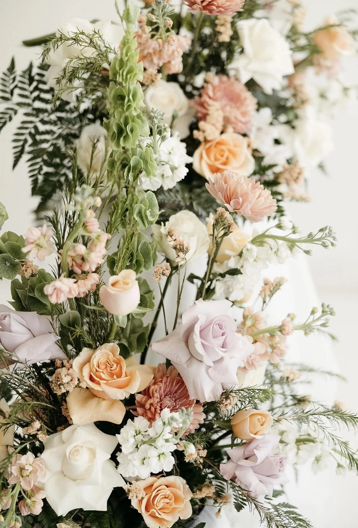 A detailed floral arrangement featuring roses, peonies, carnations, and greenery in soft pastel colors.