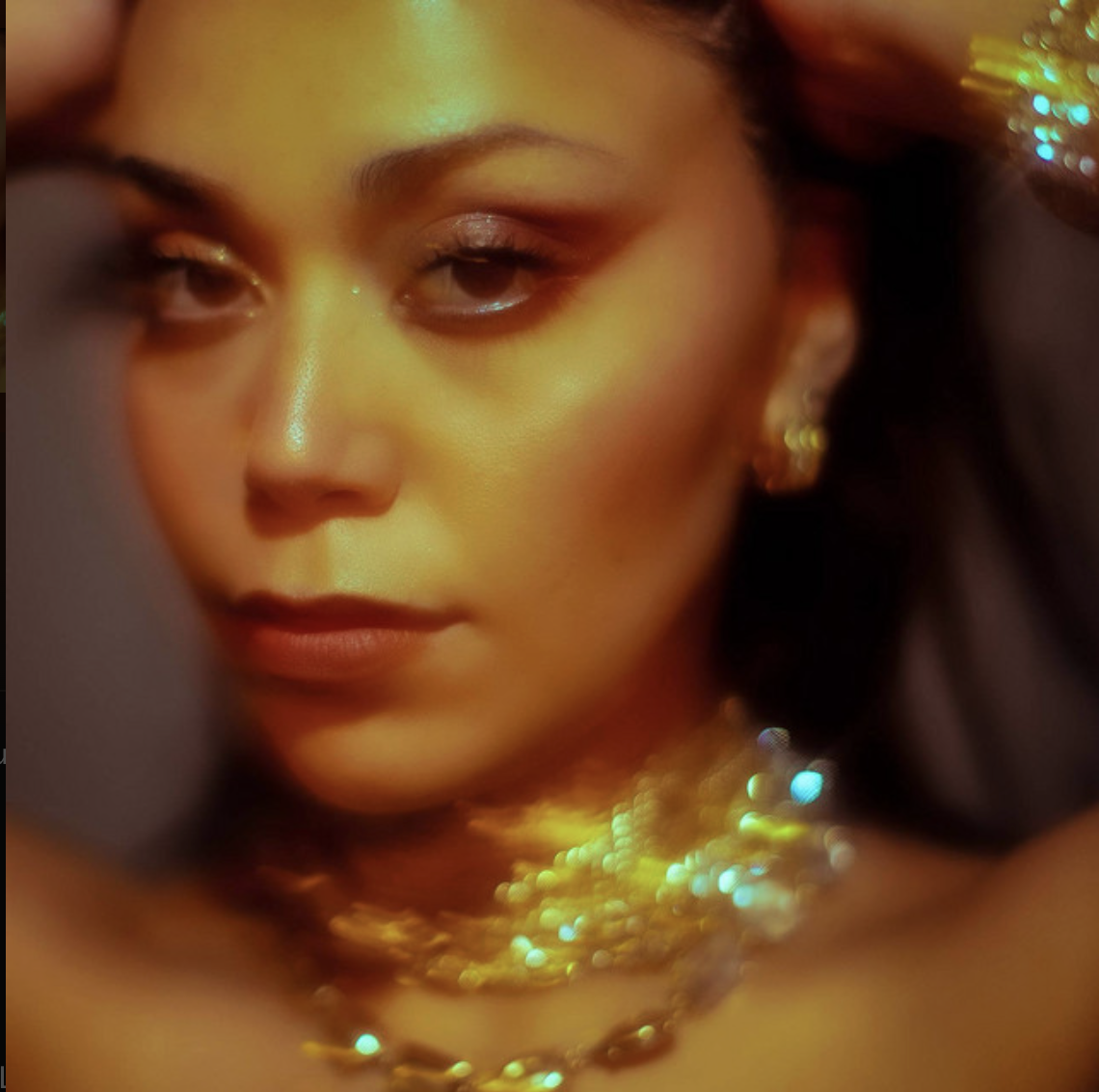 A close-up of a woman with gold jewelry and makeup, with a soft focus and warm lighting.