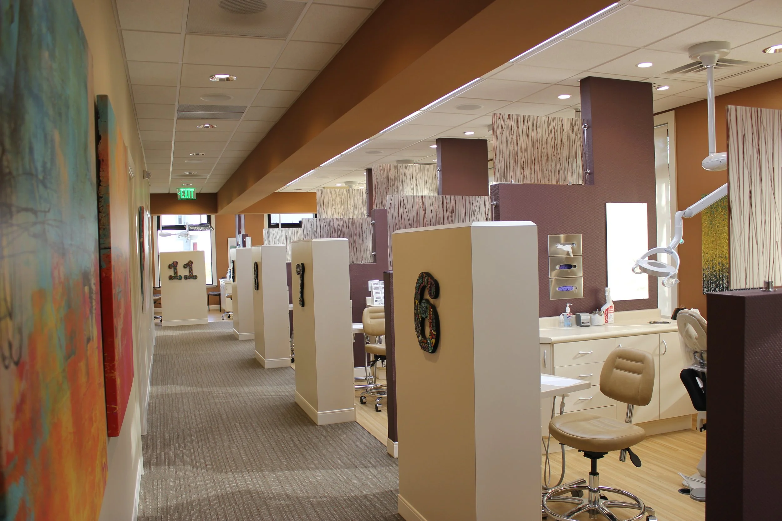 Dental clinic with individual treatment stations separated by decorative dividers, dental chairs, and clinical supplies.