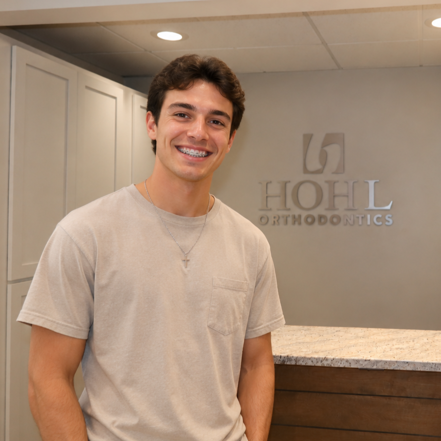 Young man with braces smiling at the reception area of a dental office, Hohl Orthodontics sign visible in the background.