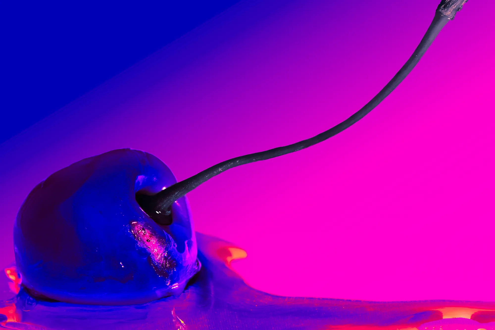 A close-up of a cherry with black stem covered in shiny, blue and purple liquid against a vibrant pink and purple background.