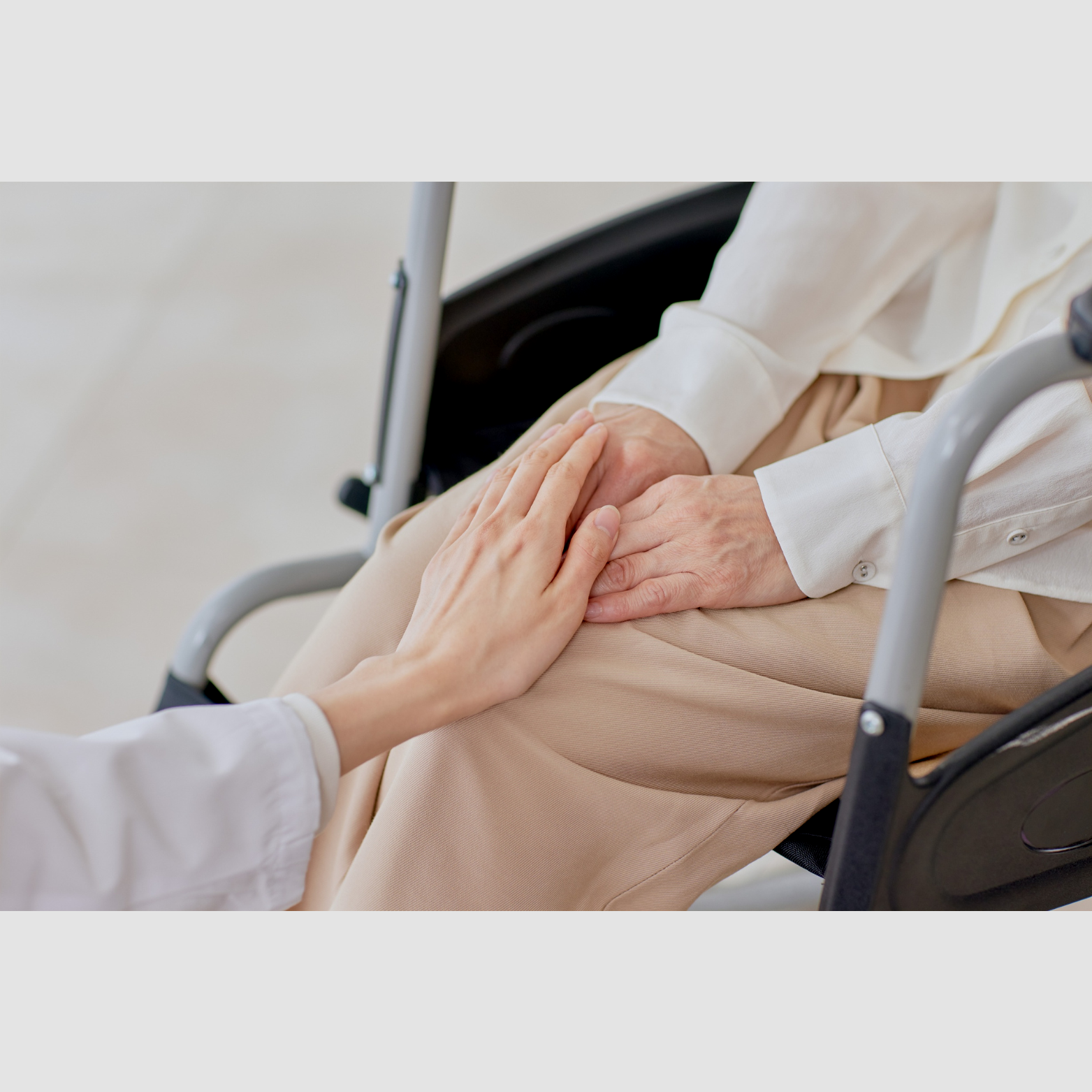 Person with a white shirt sitting in a wheelchair, holding hands with another person.