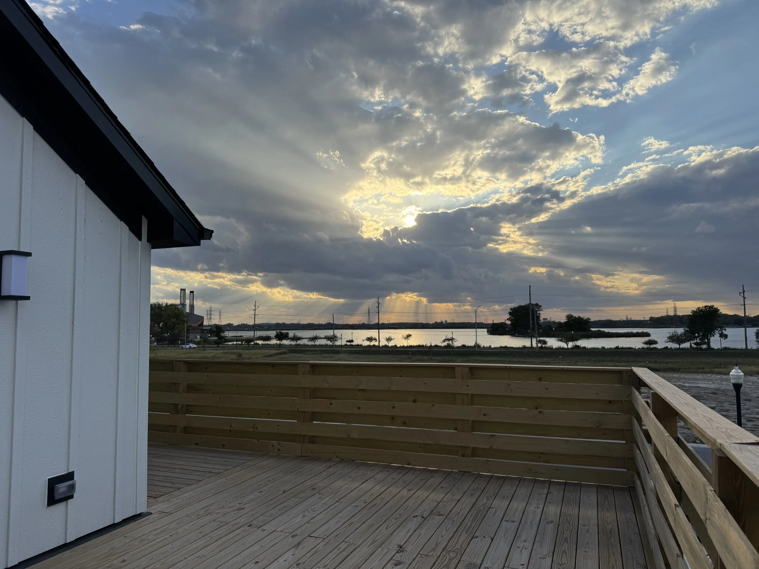 View from a wooden deck overlooking a body of water during sunset with cloudy sky.