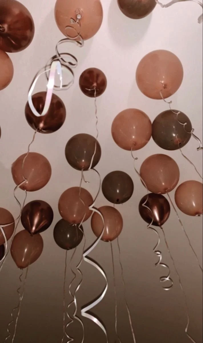 A ceiling decorated with numerous metallic bronze, copper, and rose gold balloons with curly ribbons hanging down.