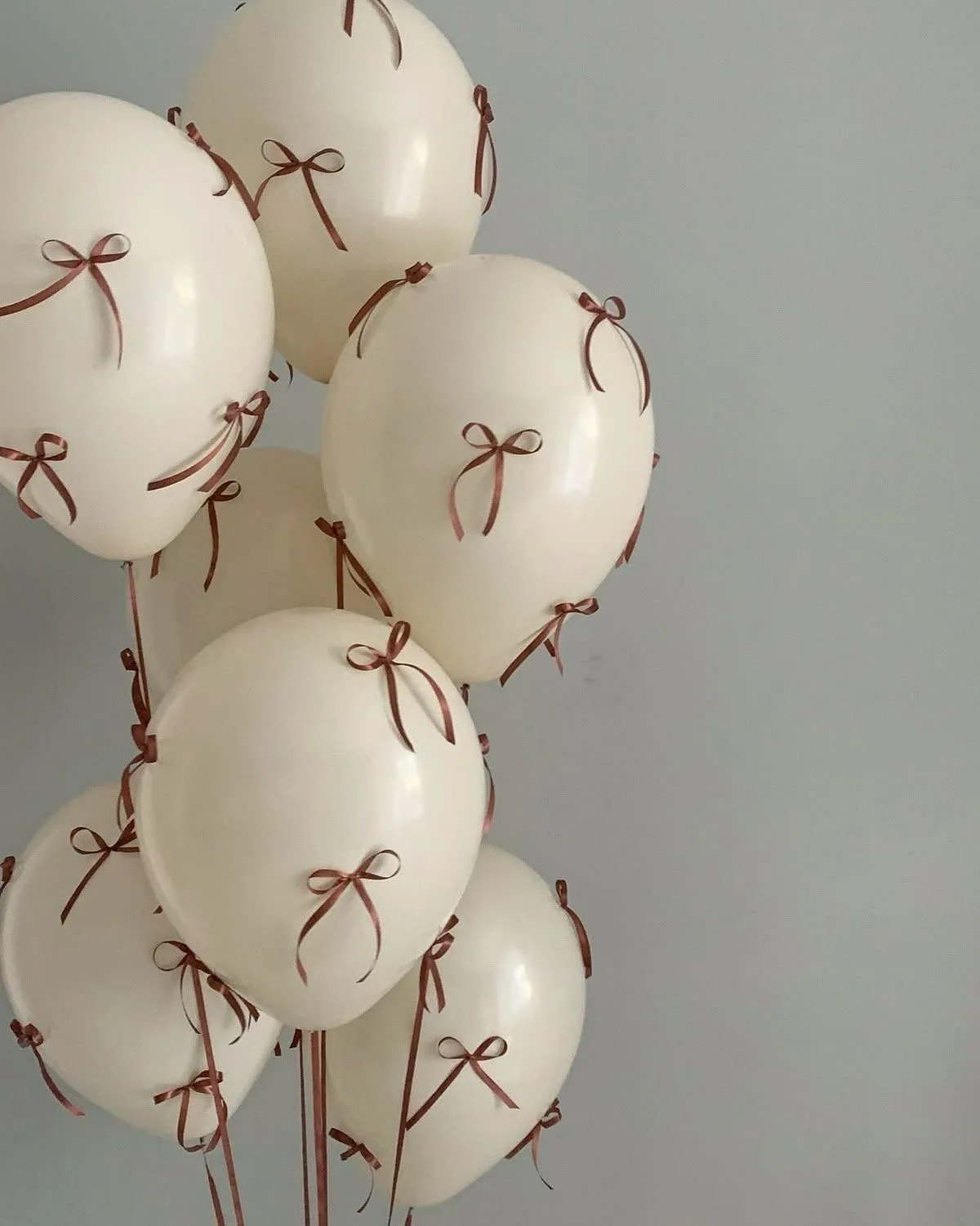 Cream-colored balloons with brown ribbons tied to them, grouped together against a plain light gray background.