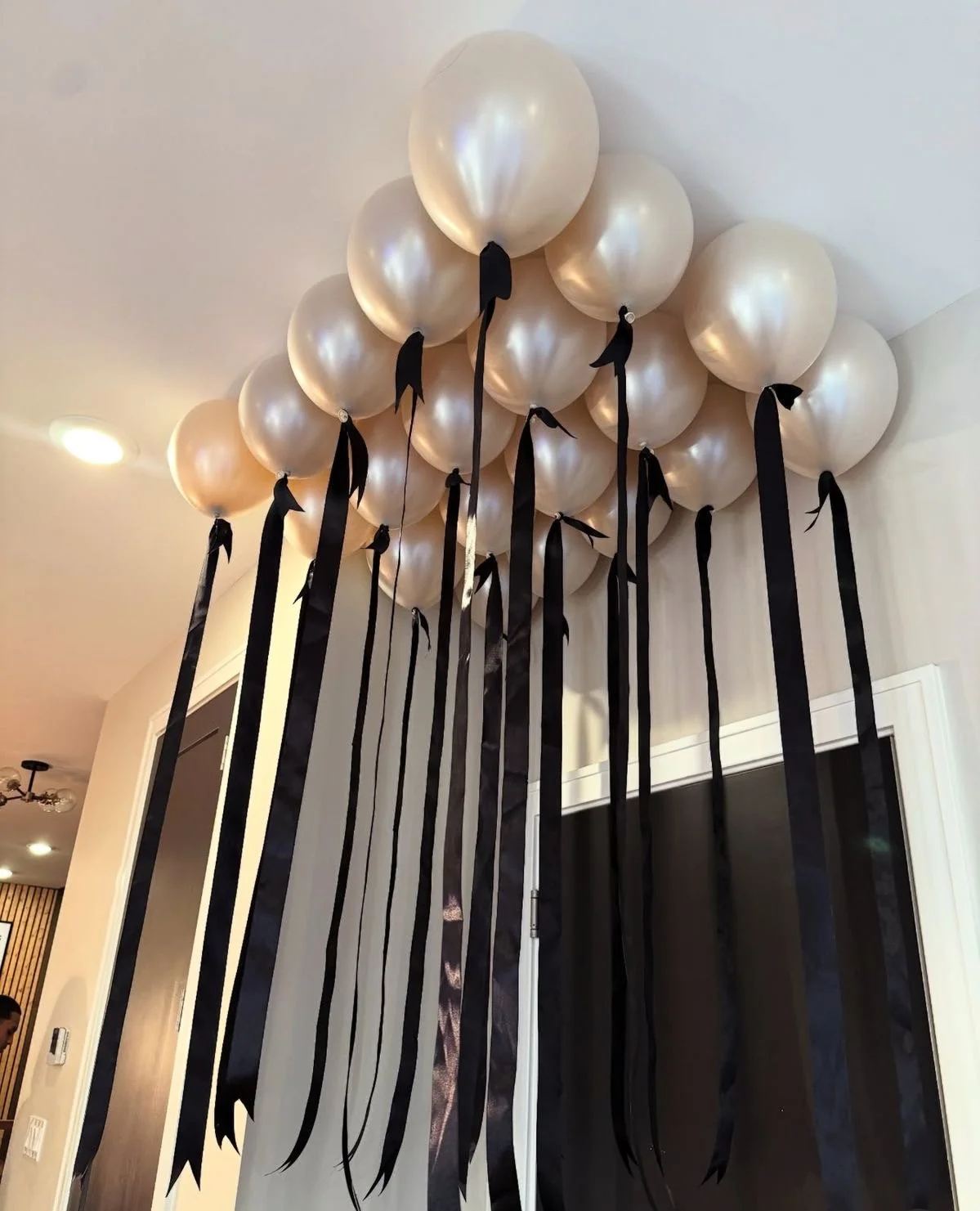 Cluster of pearl-colored balloons with long black ribbons hanging down, attached to the ceiling.