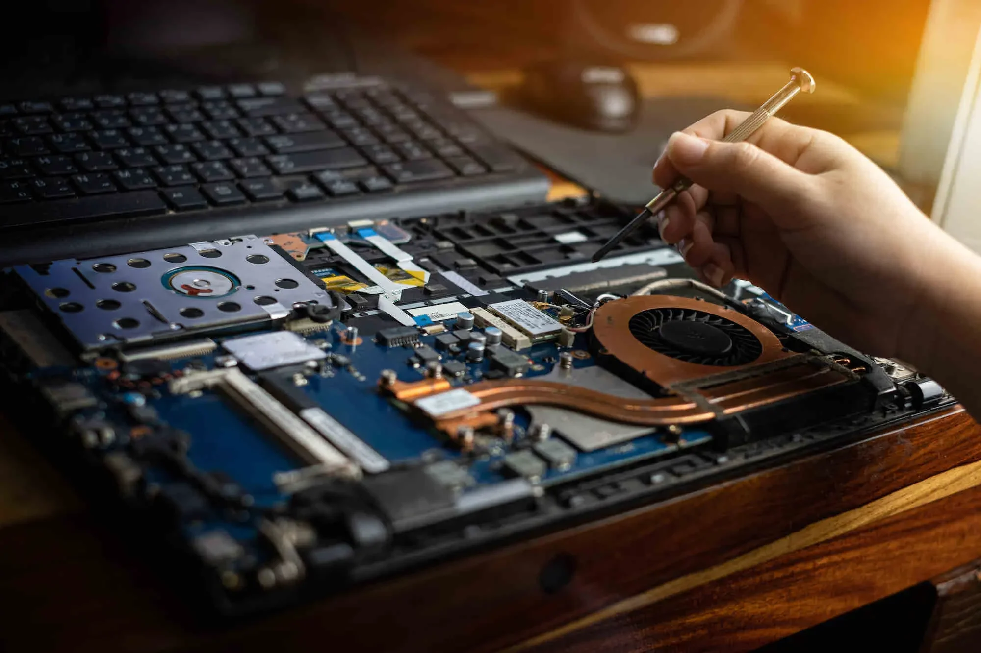 Person repairing or upgrading a laptop by working on its open internal components with a screwdriver.
