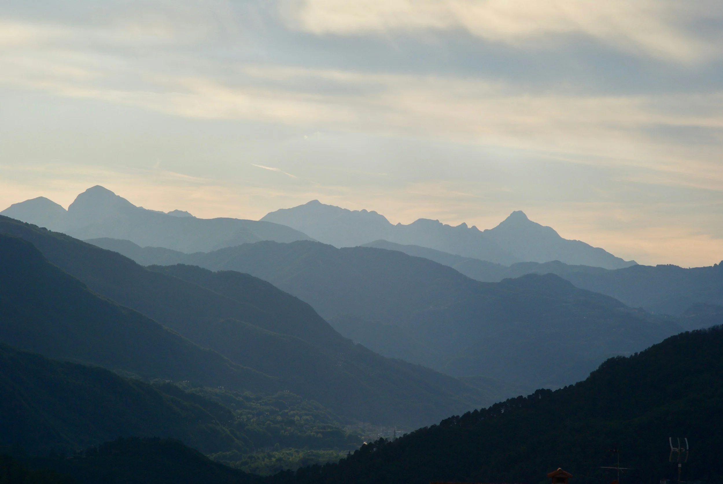 A landscape view of multiple mountain ranges in the distance under a partly cloudy sky during daytime.