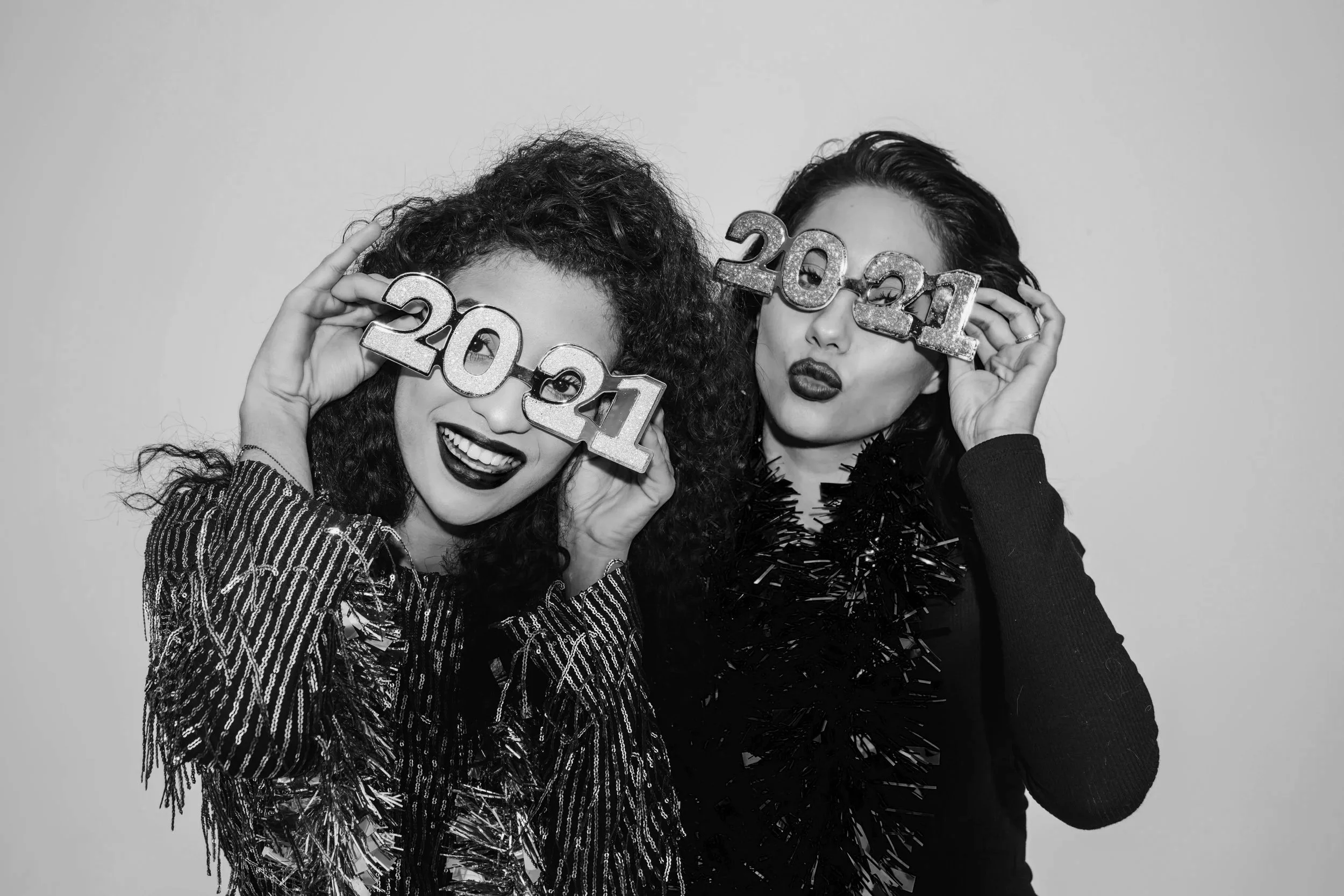 Two women wearing “2021” party glasses posing for a fun photobooth photo, representing The Shutter Spot photobooth experience.