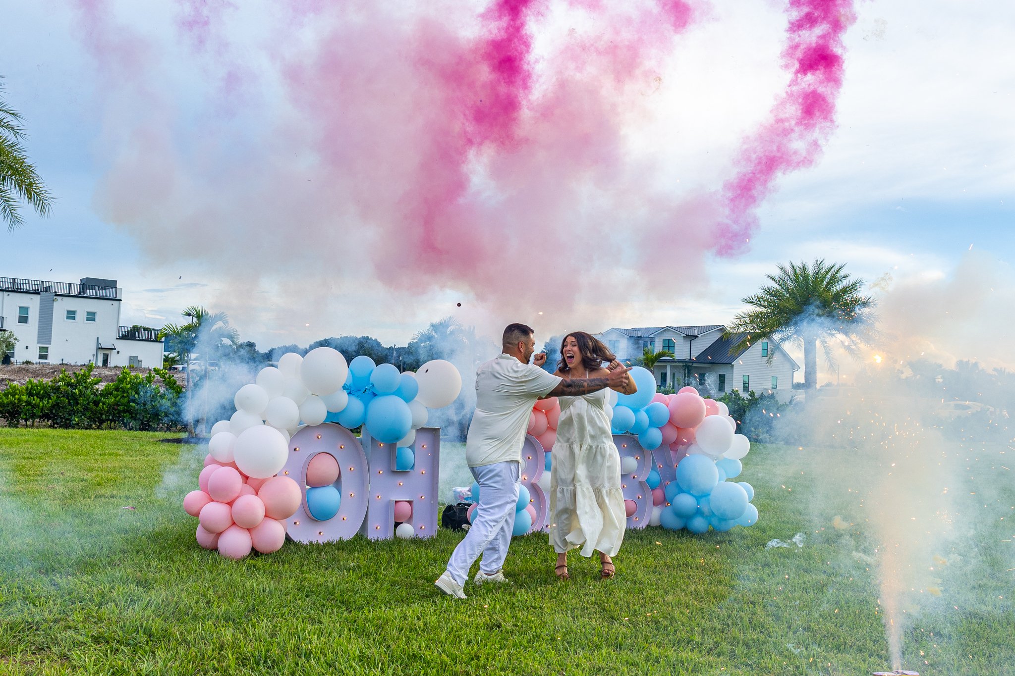 Couple celebrating outdoors with balloons and colorful smoke, laughing and dancing.