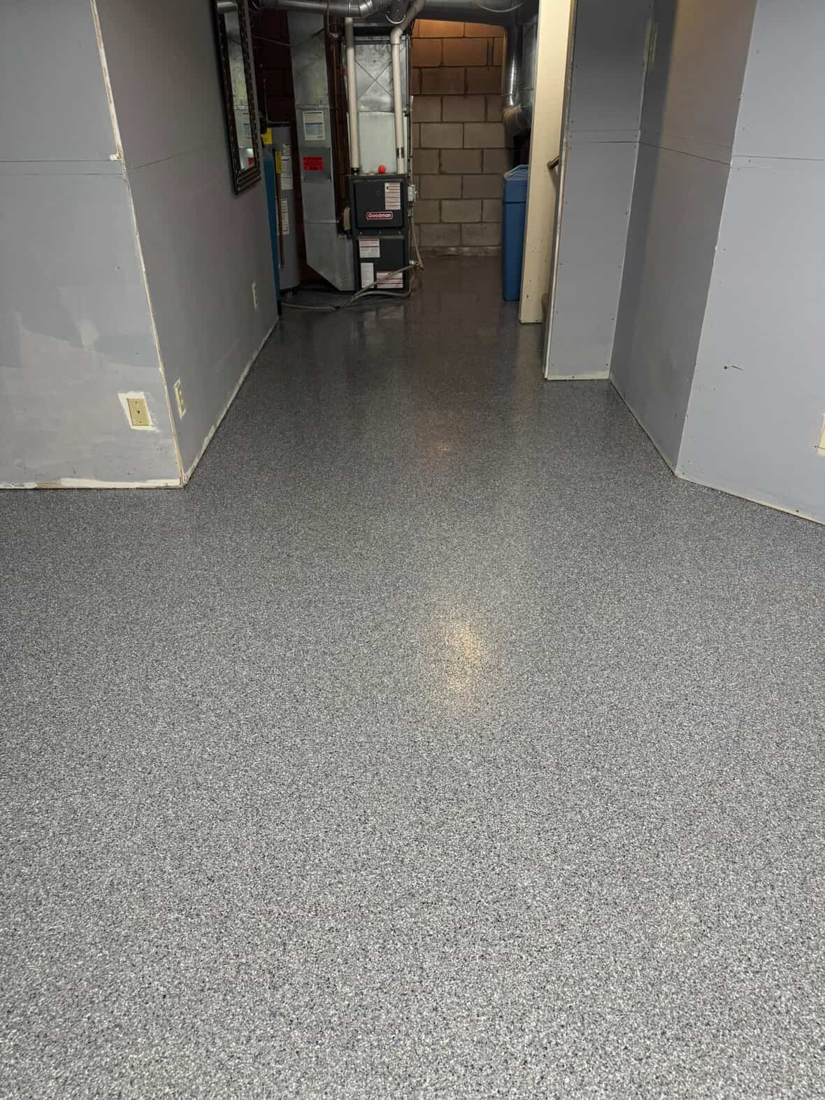 Clean, speckled gray epoxy floor in a utility or laundry room with gray painted walls and a water heater and pipes in the background.