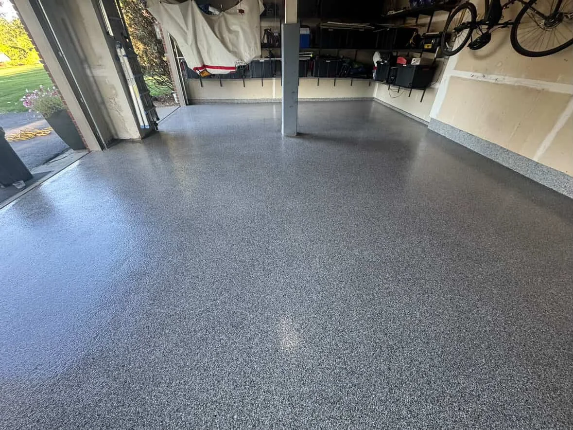 Clean, textured epoxy garage floor with an open garage door showing outside yard with flowers and garden hose.