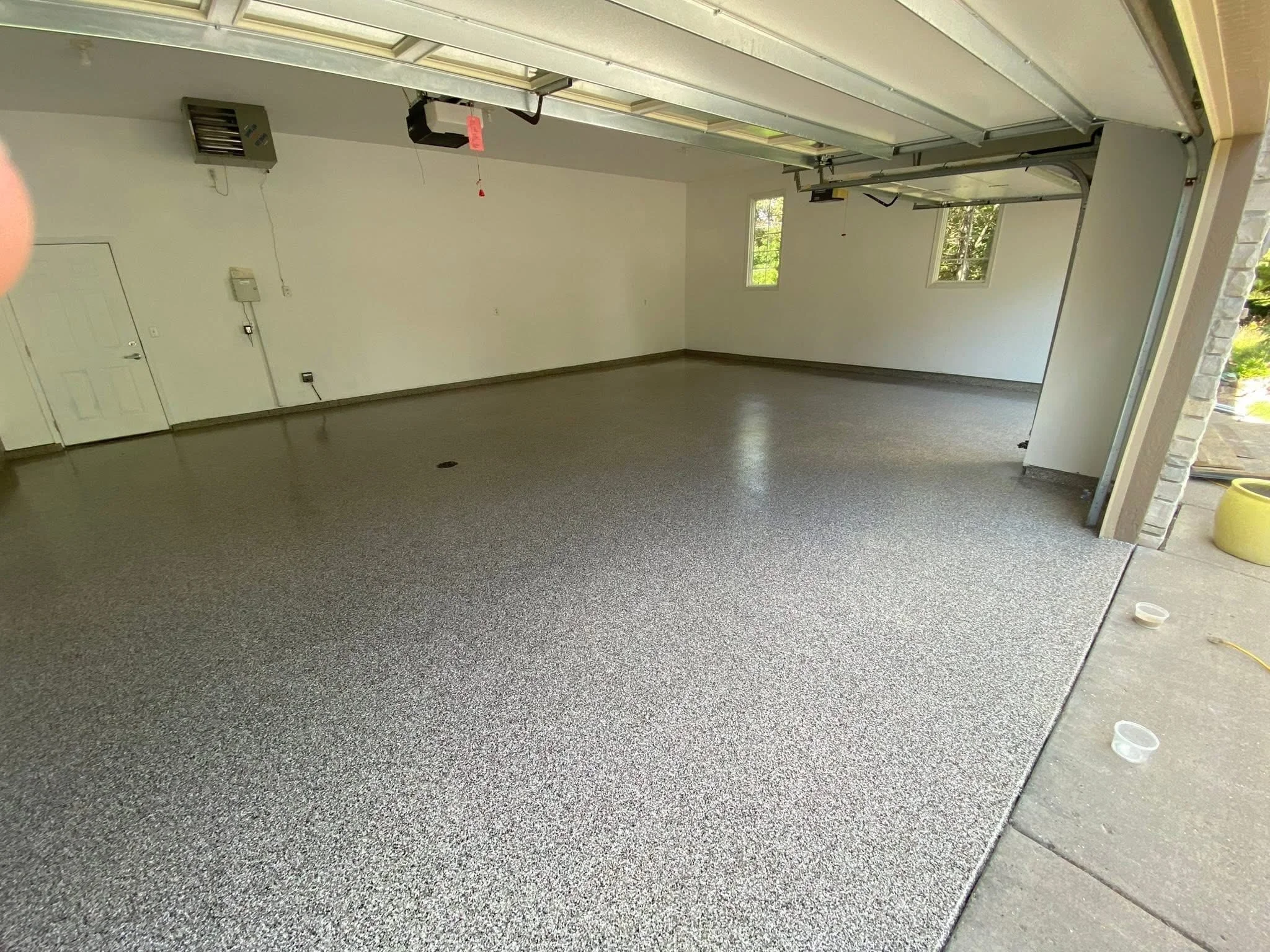 Empty garage with finished epoxy flooring, white walls, small windows, door on left, garage door open to outside, some small items on concrete outside.