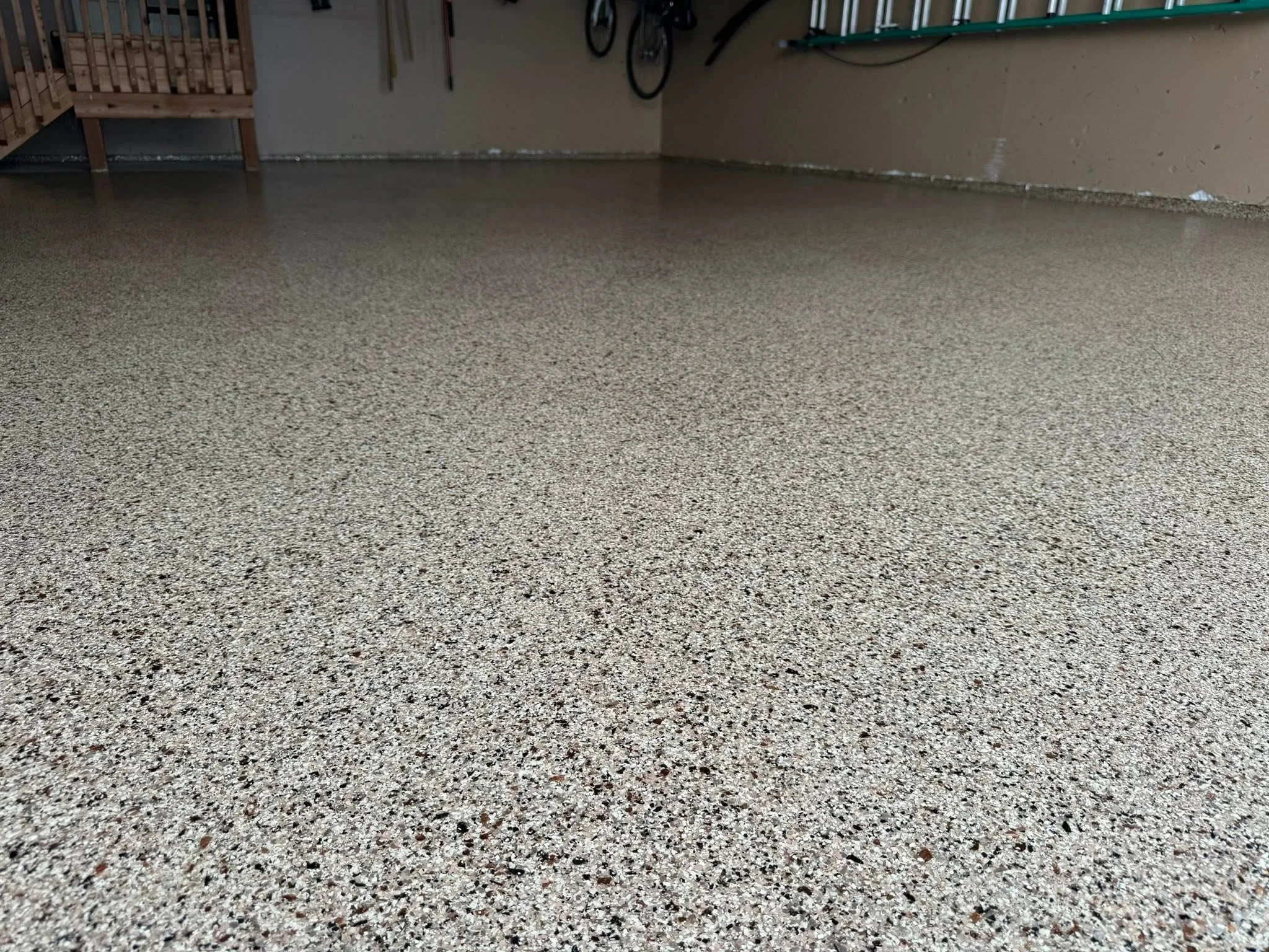 A newly finished speckled epoxy garage floor with bicycle wall hooks and storage shelves in the background.