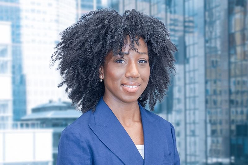 Professional woman with natural curly hair wearing a blue blazer standing in front of a city office building.