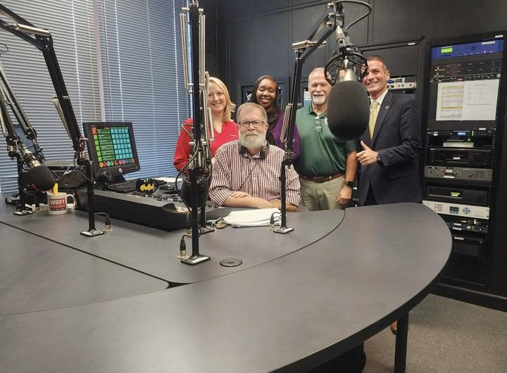 Dr. Trevor Ivey smiles with a radio host and community partners inside a recording studio after discussing education-related topics.